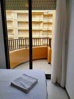 A balcony with a bed and a folded towel, overlooking a multi-story building with balconies. - Tamaris playa 6ºD Solo Familias! (Xeraco Playa)