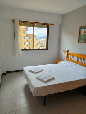 A bedroom with a bed, a window with a view of buildings, and a painting on the wall. - Tamaris playa 6ºD Solo Familias! (Xeraco Playa)