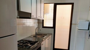 Une cuisine de taille réduite avec des meubles blancs, une cuisinière à gaz, un évier et un four à micro-ondes.