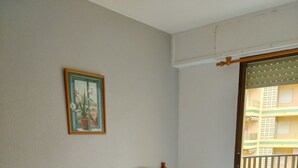 Une chambre d’hôtel avec deux lits simples, une tête de lit en bois, une table de chevet, un tableau au mur et un balcon avec vue sur un immeuble.