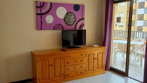 Een kamer met een houten kast, een flatscreentelevisie en een groot raam met uitzicht op een balkon.