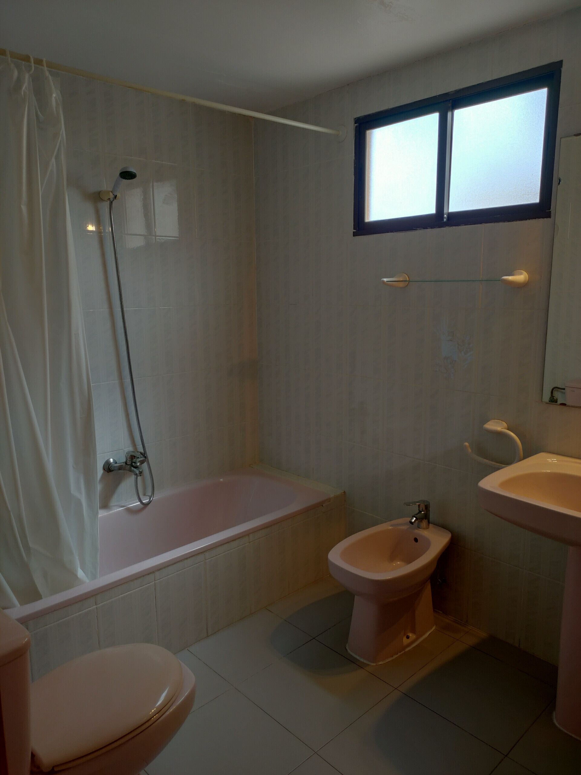Een badkamer met een bad, een toilet, een wc en een raam.