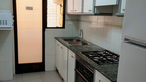 Een kleine keuken met witte kastjes, een roestvrijstalen spoelbak, een gasfornuis en een inbouwoven.