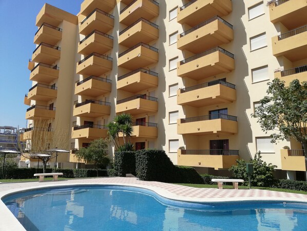 A multi-story residential building with balconies, a swimming pool, and surrounding greenery.