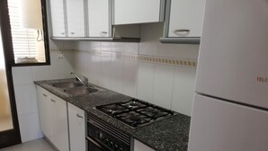 Eine Küche mit weißen Schränken, einem Gasherd, einer Spüle und einem Kühlschrank.