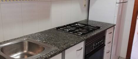 A kitchen with white cabinets, a granite countertop, a stainless steel sink, a gas stove, and a white refrigerator.