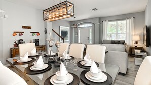 Un espace de salle à manger moderne avec une table en verre pouvant accueillir six personnes, un lustre et une vue sur le salon.