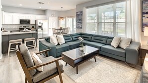 Un salon moderne avec un canapé d’angle, une table basse et un coin repas agrémenté d’un lustre.