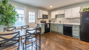 A modern kitchen with light green cabinets, a black refrigerator, and a dining area with wooden chairs and a table. - Cozy Connected Duplex Home with Driveway (Atlanta)