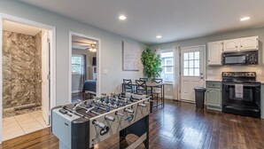 A spacious room with a foosball table, a dining area with chairs, a kitchen with cabinets and appliances, and a stone wall. - Cozy Connected Duplex Home with Driveway (Atlanta)