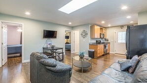 A modern living room with a sofa, coffee table, and a TV. A kitchen is visible in the background with wooden cabinets and a microwave. - Cozy Connected Duplex Home with Driveway (Atlanta)