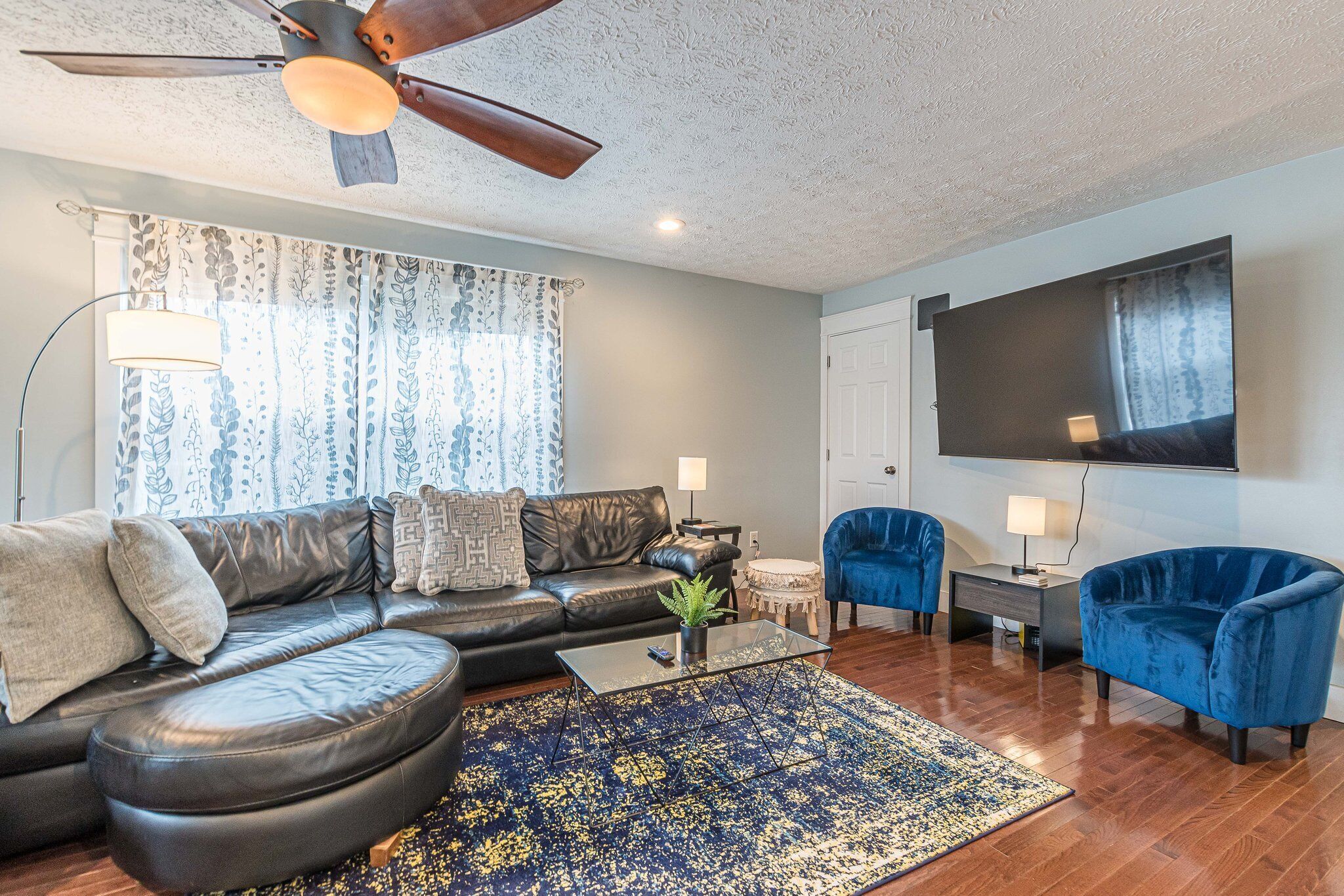 A modern living room with a leather sofa, a blue armchair, a coffee table, and a ceiling fan.