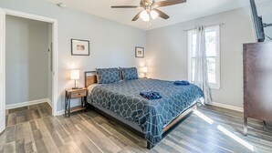A bedroom with a bed, ceiling fan, bedside lamps, and a window with curtains.