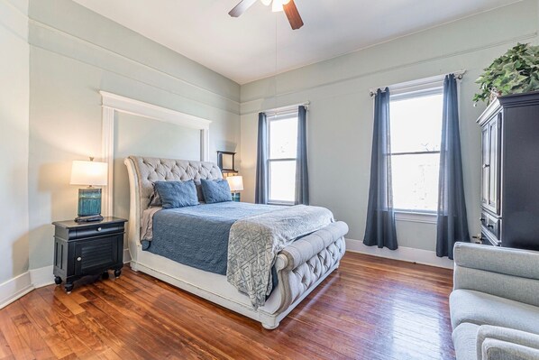 Un dormitorio con una cama grande, una mesita de noche, un aparador y una ventana con cortinas.