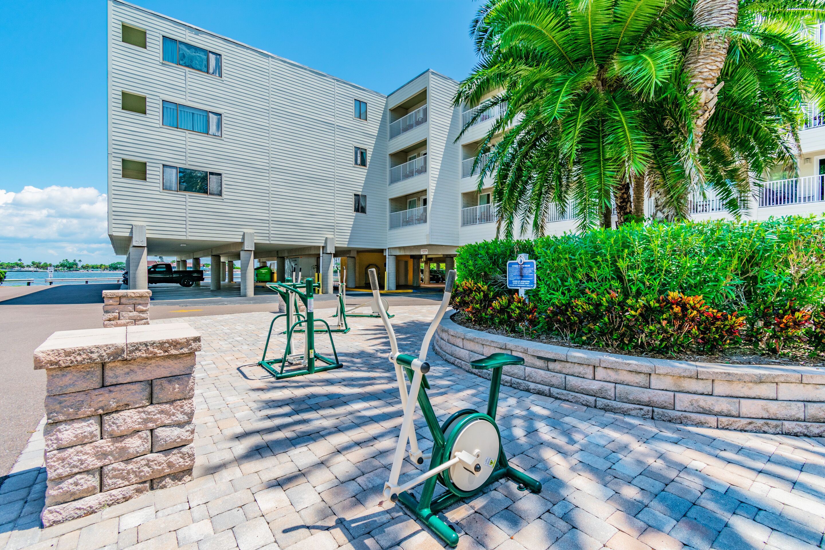 A modern building with multiple floors, outdoor exercise equipment, and a landscaped area with palm trees.