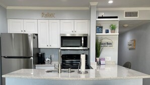Una cocina moderna con armarios blancos, electrodomésticos de acero inoxidable y una isla central con dos taburetes de bar.