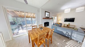 Uma sala de estar com lareira, televisão fixada na parede e um espaço de jantar com mesa e cadeiras de madeira.