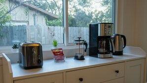 Uma bancada de cozinha com uma torradeira, uma cafeteira, uma prensa francesa e um saco de café.