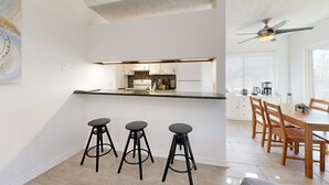 Cozinha moderna com ilha central, três bancos pretos e área de refeições com cadeiras de madeira e uma mesa.
