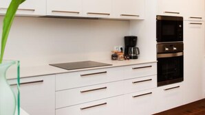 Una cuina moderna amb armaris blancs, forn negre i cafetera.