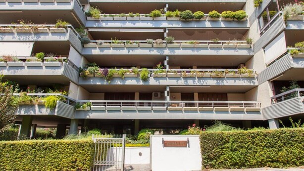Edifici d'apartaments de diversos pisos amb balcons, cadascun decorat amb plantes.