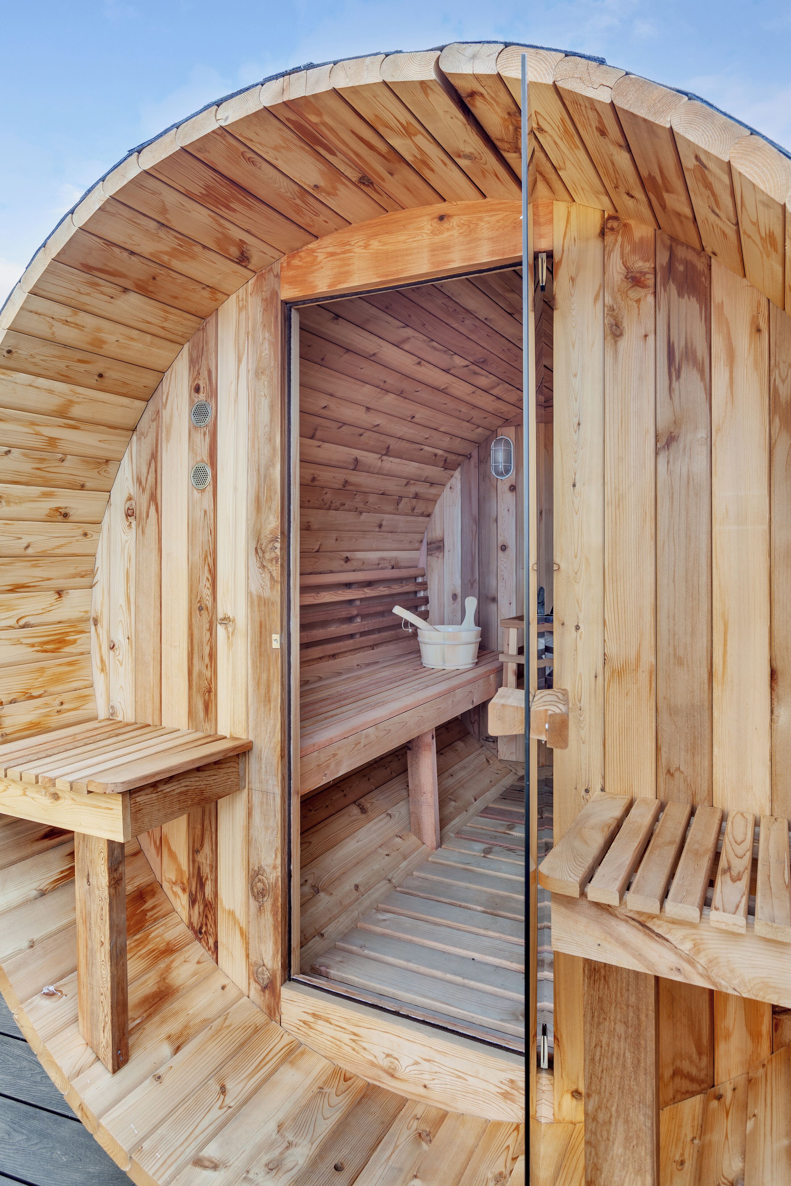 Un sauna en bois avec un banc et une banquette, une porte en bois et un banc doté d’un dossier.