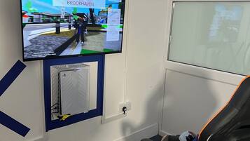 Une pièce équipée d’un téléviseur fixé au mur qui affiche un environnement virtuel, d’un fauteuil de jeu et d’une fenêtre.