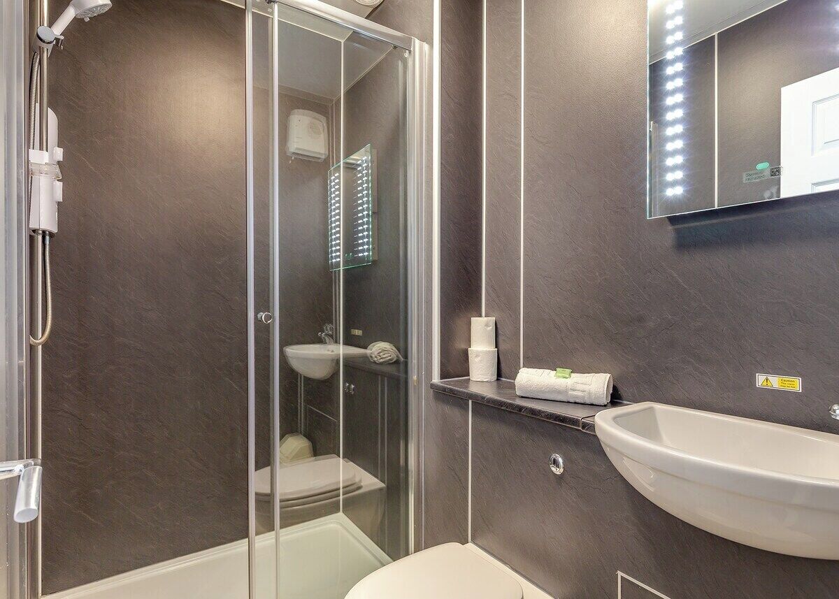 A modern bathroom with a glass-enclosed shower, a white sink, and a mirror with lights.