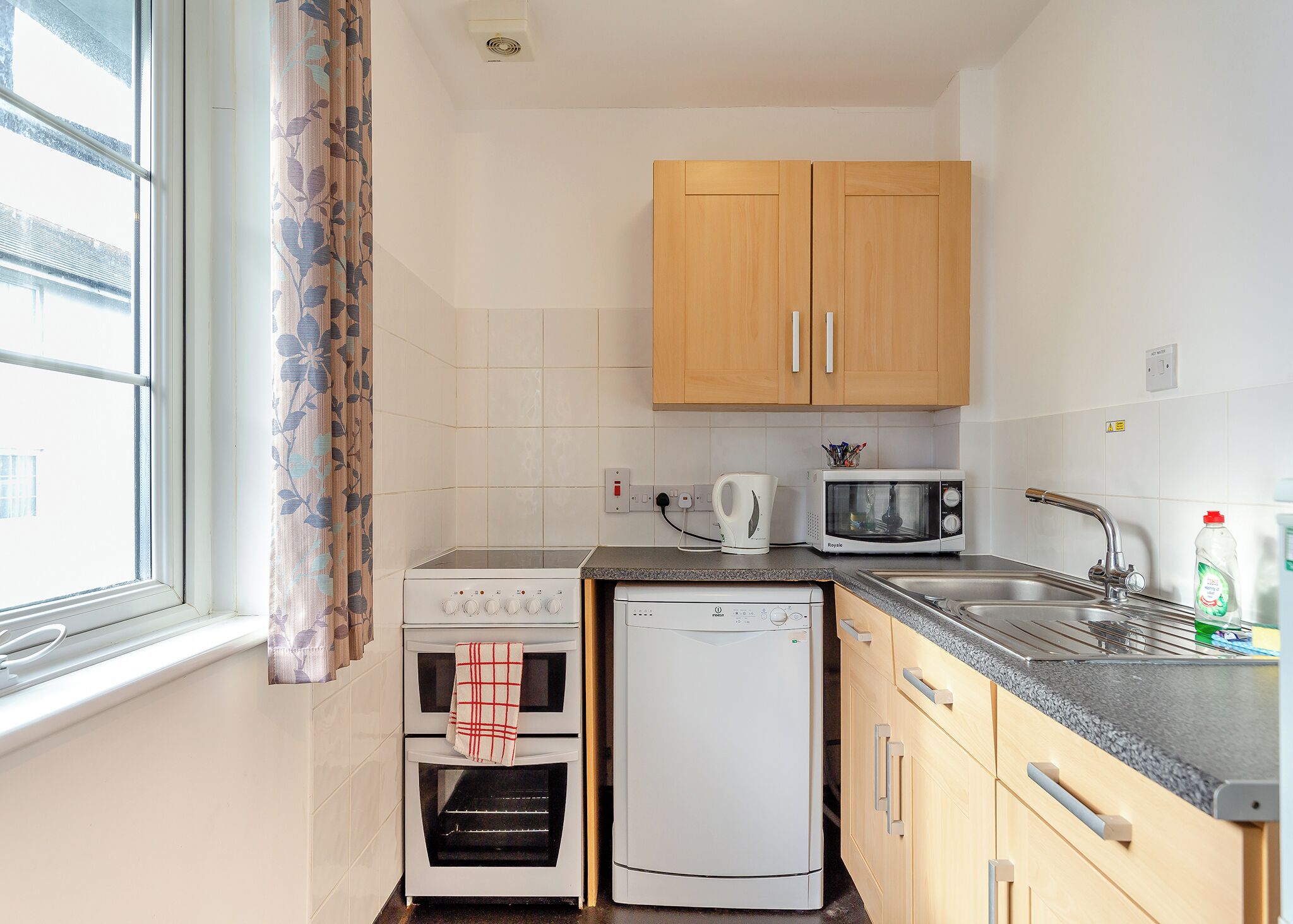 A compact kitchen with a stove, microwave, dishwasher, and wooden cabinets.