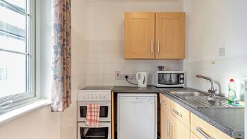 A compact kitchen with a stove, microwave, dishwasher, and wooden cabinets.