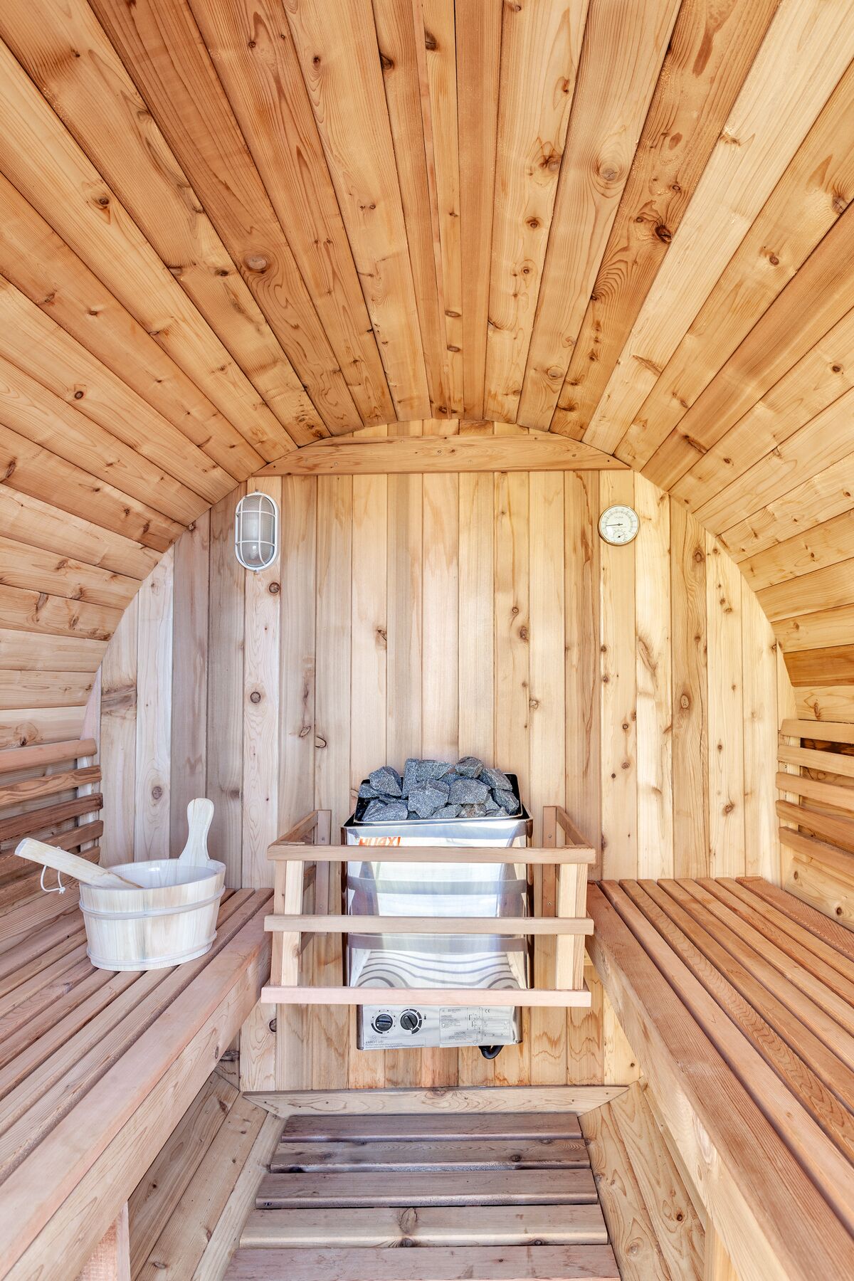A sauna with wooden walls and benches, a heater, and a bucket.