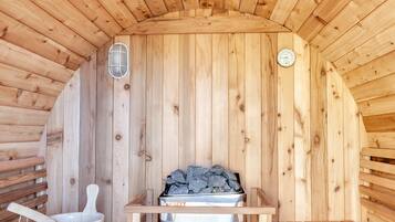 Una sauna amb parets i bancs de fusta, un escalfador i un cubell.