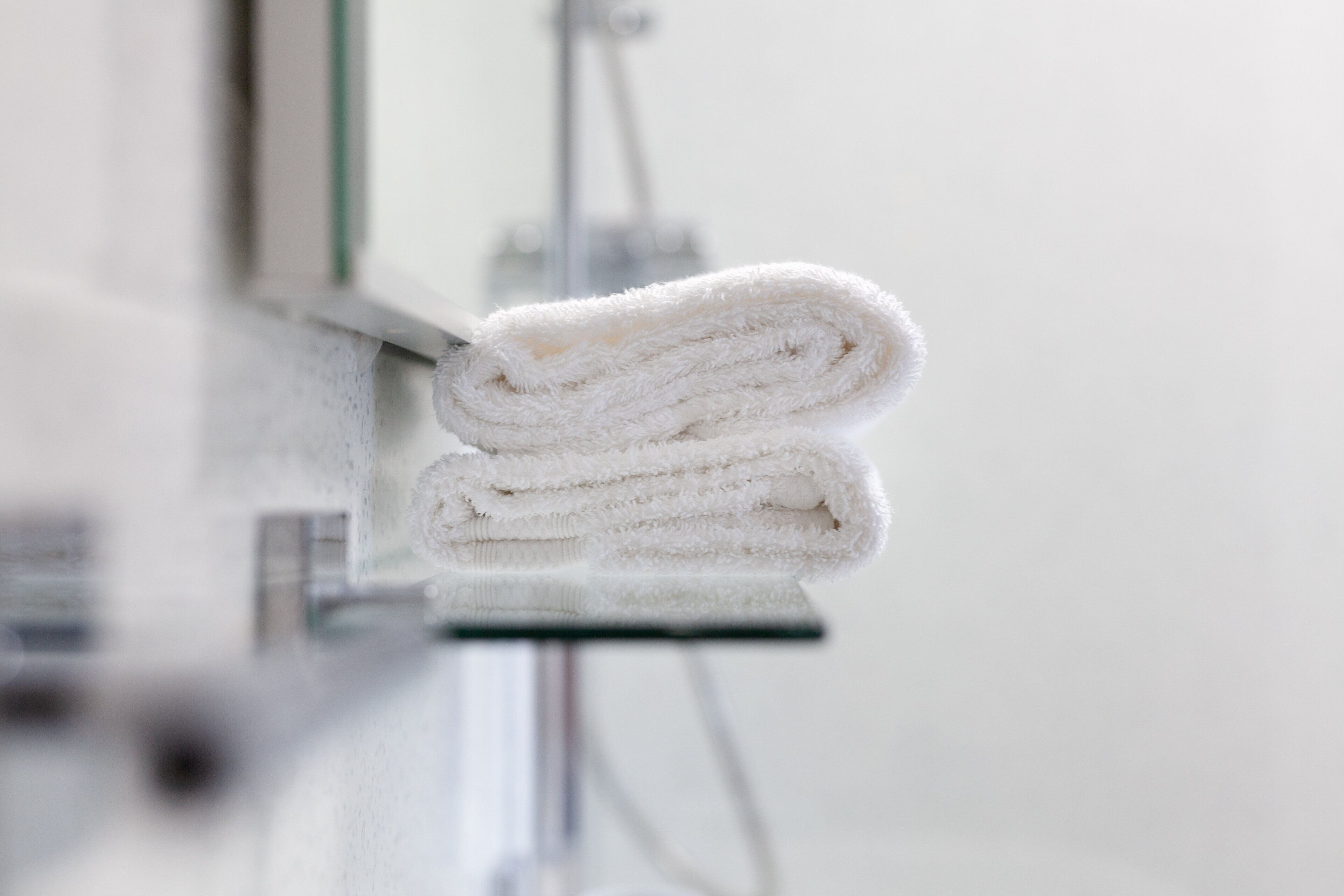 A folded white towel on a glass surface, likely in a hotel room.