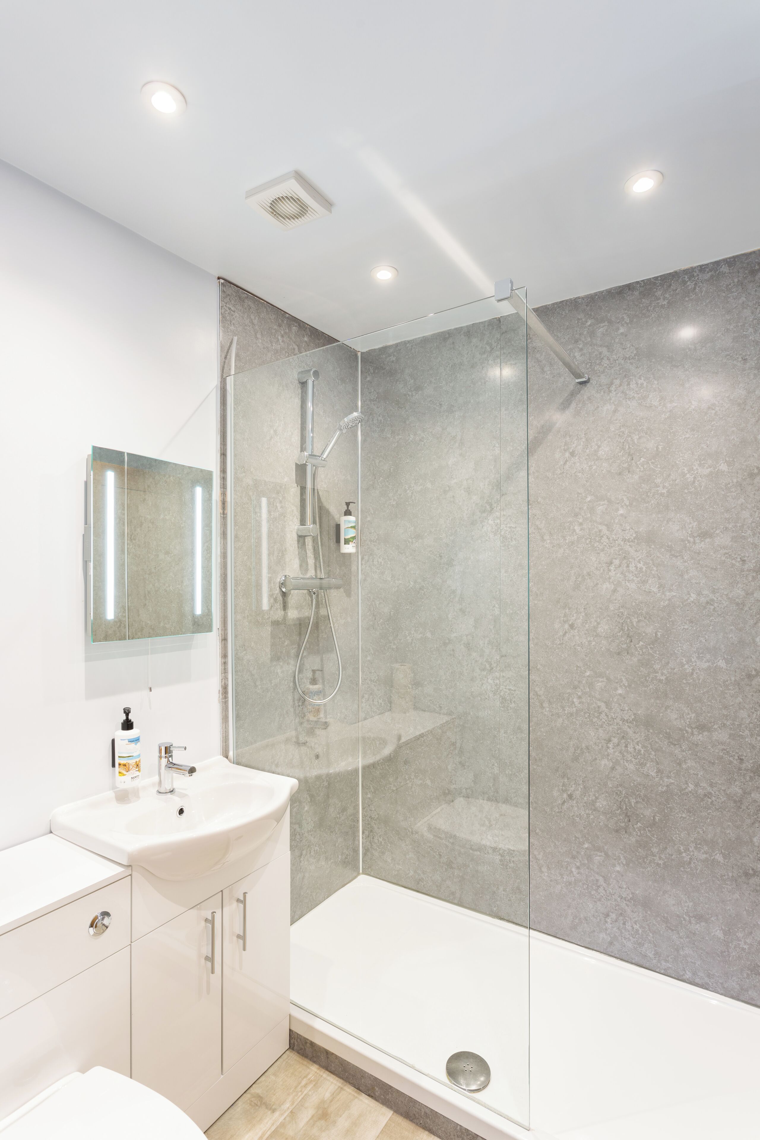 Un baño moderno con ducha de vidrio, un lavabo blanco y un espejo.