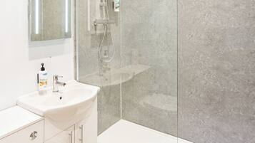Un baño moderno con ducha de vidrio, un lavabo blanco y un espejo.