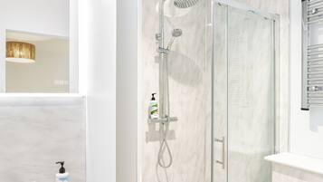 Un baño moderno con ducha de vidrio, lavamanos blanco y retrete.