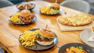 A wooden table with various dishes including burgers, fries, and a pizza.