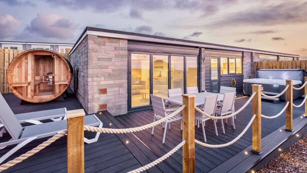 A modern outdoor deck with a wooden sauna, a brick wall, and a hot tub. - Hot Tub Haven with Dreamy Sea Vista! (Ilfracombe)