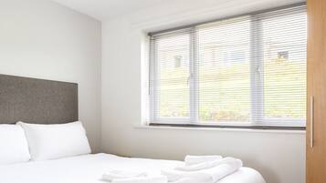 Una habitación de hotel moderna con una cama grande, cabecera gris, una ventana con persianas y un armario de madera.