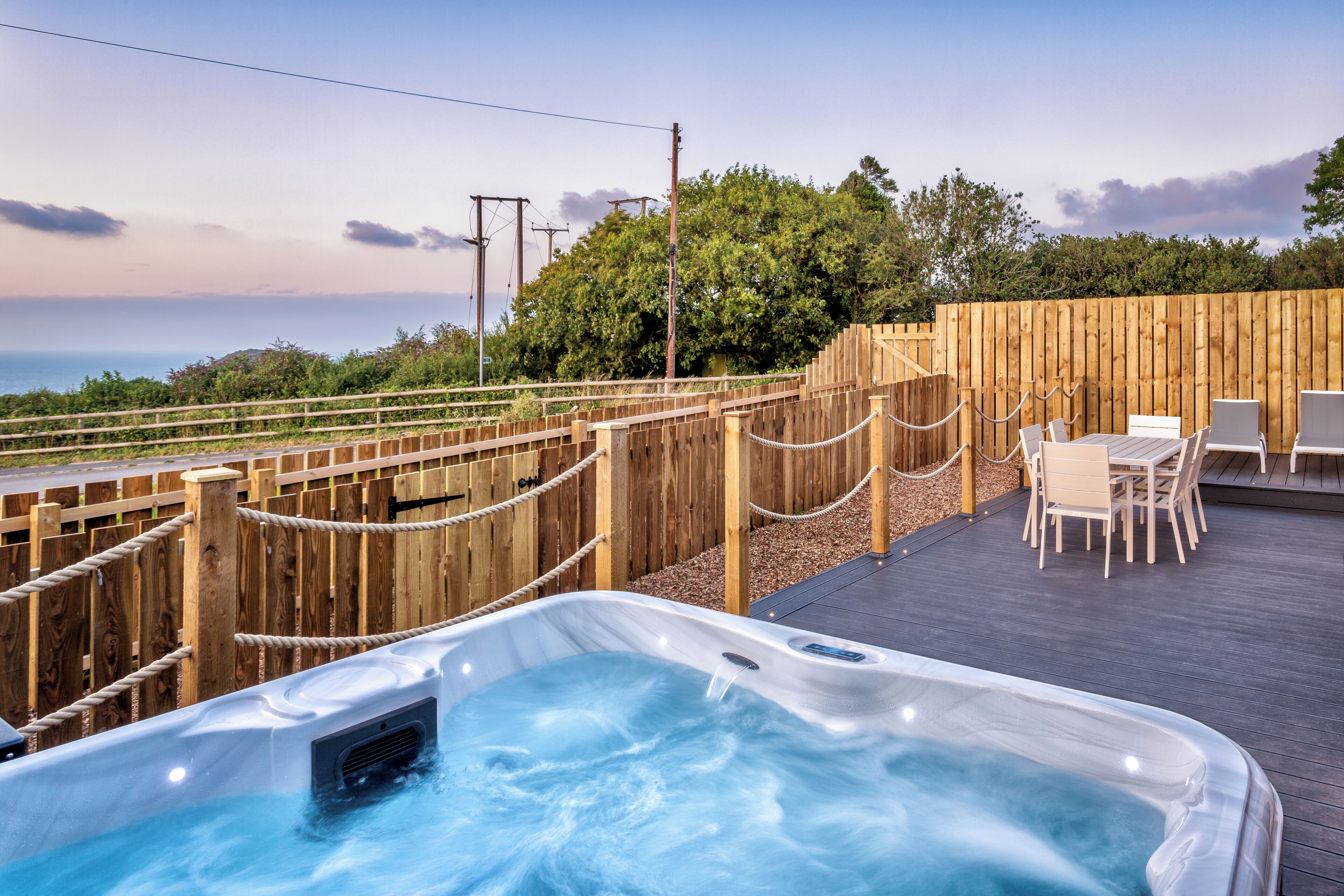 A hot tub on a wooden deck with a view of the ocean.