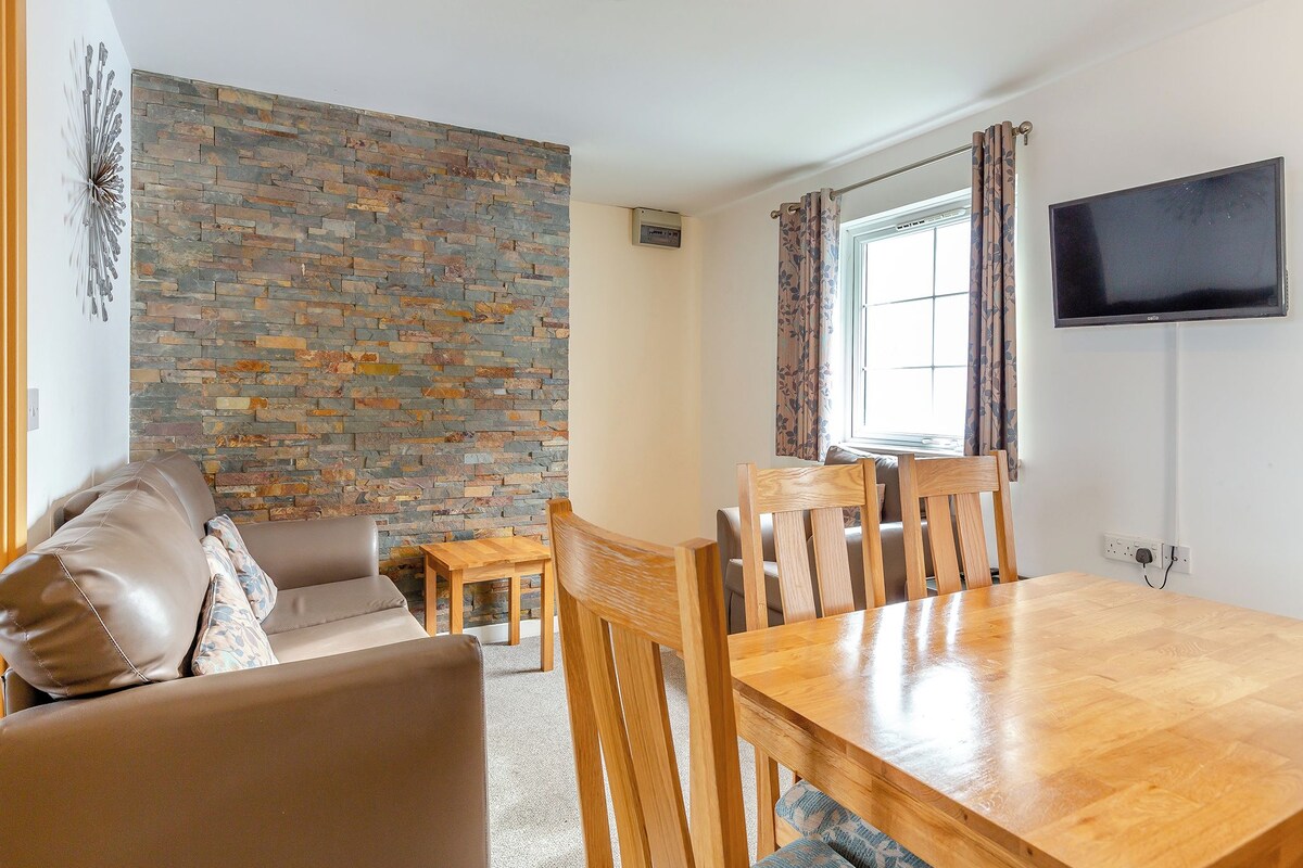 A cozy living room with a stone wall, a wooden dining table, and a flat-screen TV.