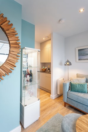 A modern living room with a glass cabinet, a blue sofa, and a wooden wall decor. - NDR Residencies (Ilfracombe)