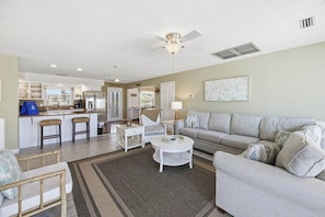 A spacious living area with a sofa, coffee table, and a dining area with chairs and a kitchen in the background. - Sanderley | Canalfront | Fire Pit, Private Dock (Virginia Beach)