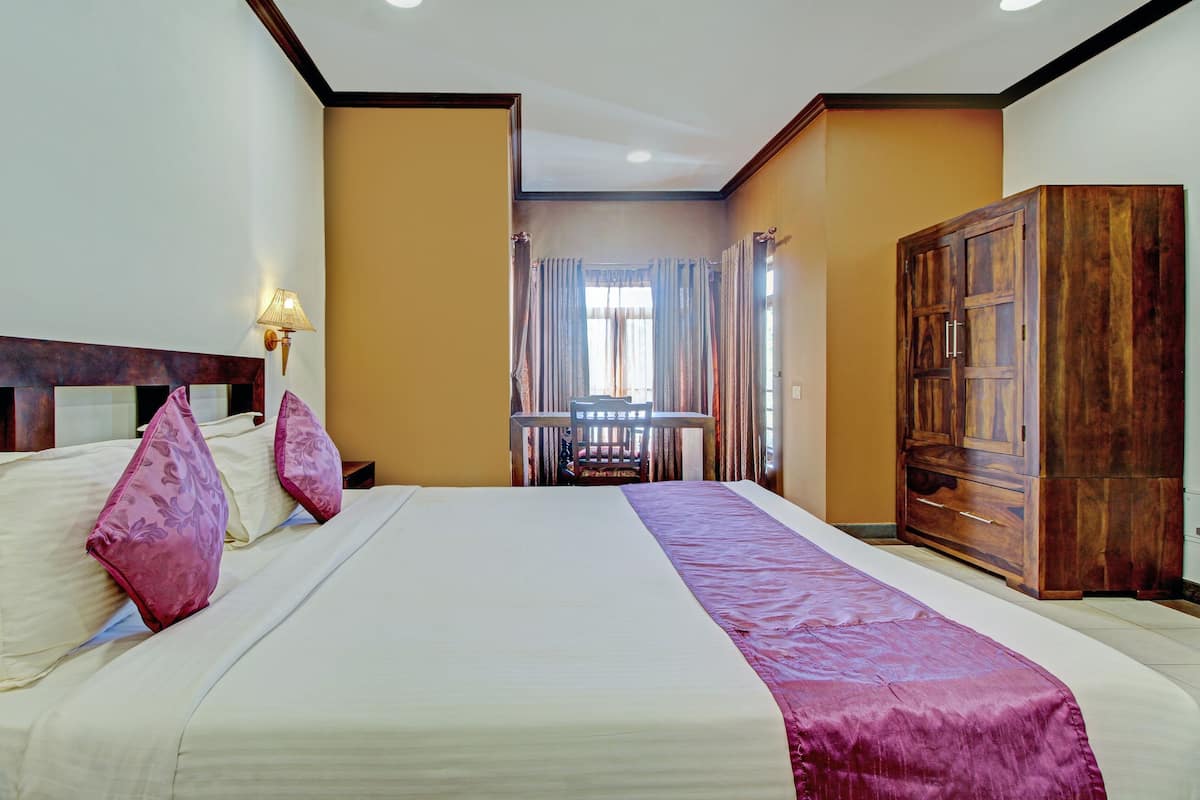A hotel room with a large bed, a wooden wardrobe, and a small table with a chair.