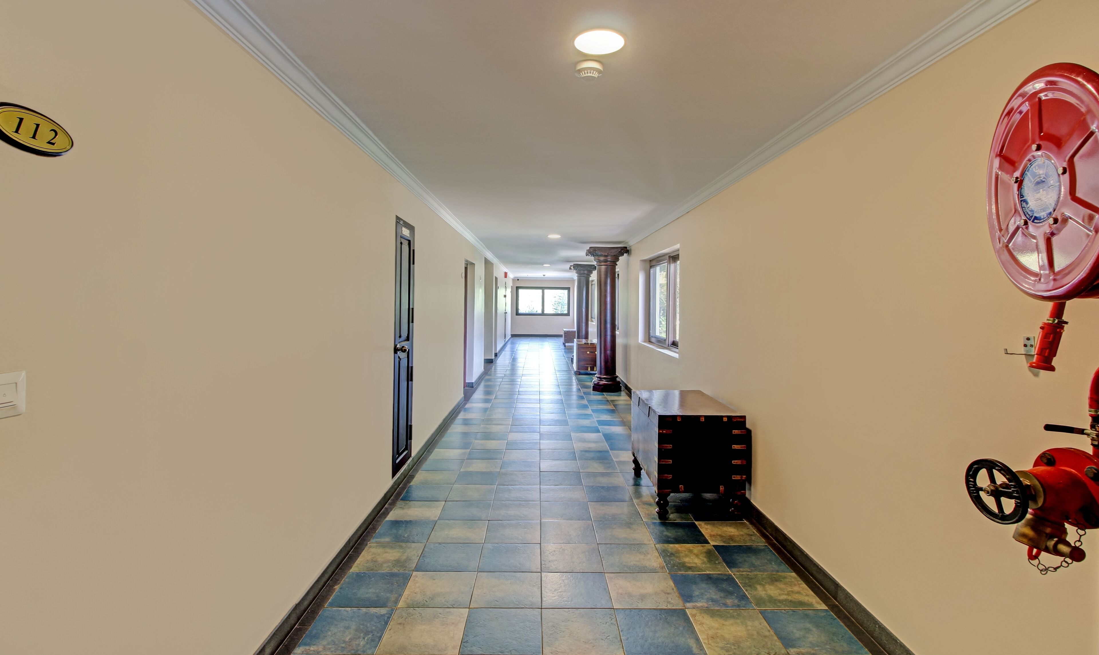 A hallway with a checkered floor, a fire extinguisher on the right, and a door on the left.