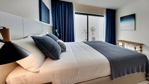 Une chambre à coucher moderne avec un grand lit, une lampe de chevet et une vue sur l’extérieur par une fenêtre.