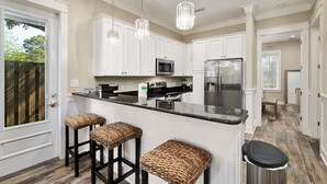 Une cuisine moderne avec des meubles blancs, un plan de travail noir et deux tabourets en osier.