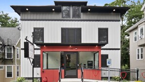 Un edificio moderno con una entrada roja, una rampa accesible para sillas de ruedas y un cartel que indica estacionamiento reservado.