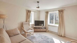 A modern living room with a sofa, armchair, TV, and a fireplace. - Host & Stay | 57 Woodland View (Holmfirth)