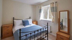 A bedroom with a bed, bedside tables, a window with curtains, a radiator, and a mirror. - Host & Stay | 57 Woodland View (Holmfirth)